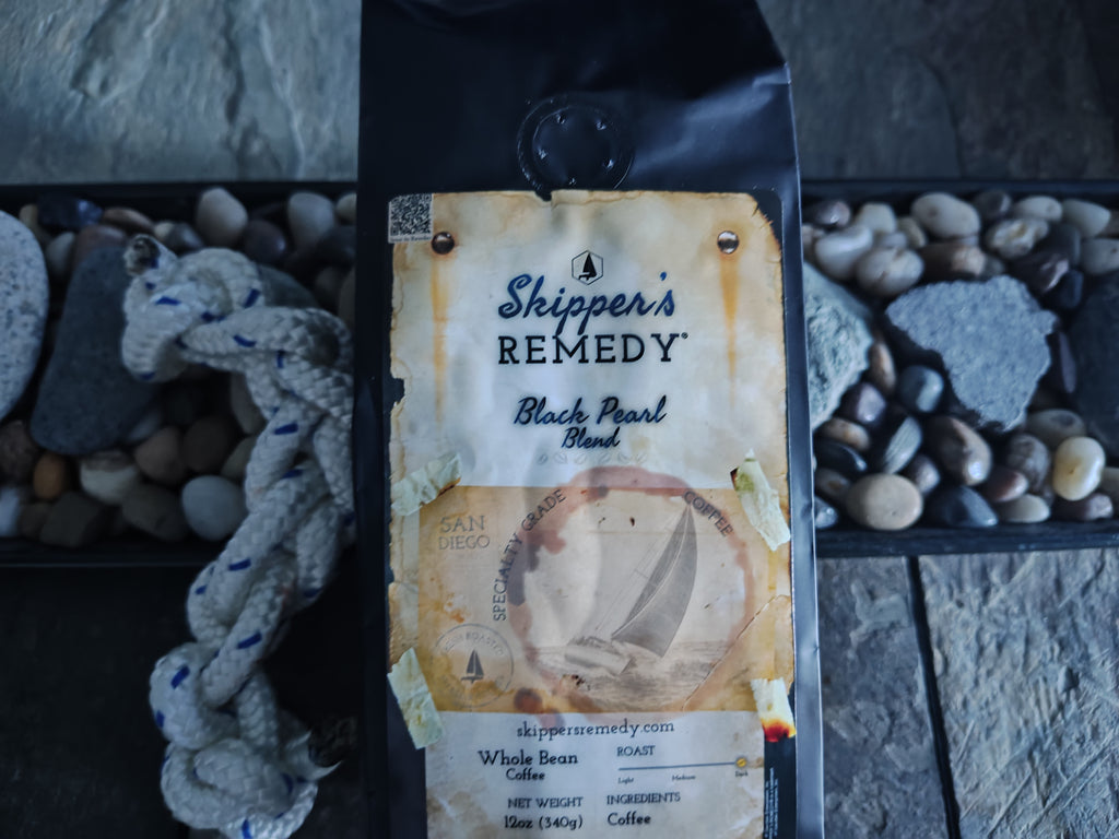 Skipper's Remedy Black Pearl Blend coffee, with a sailboat design on a stone surface.