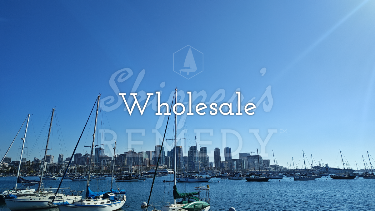 Marina with sailboats and city skyline under a clear blue sky, featuring the text 'Wholesale' and 'Skipper's Remedy'.